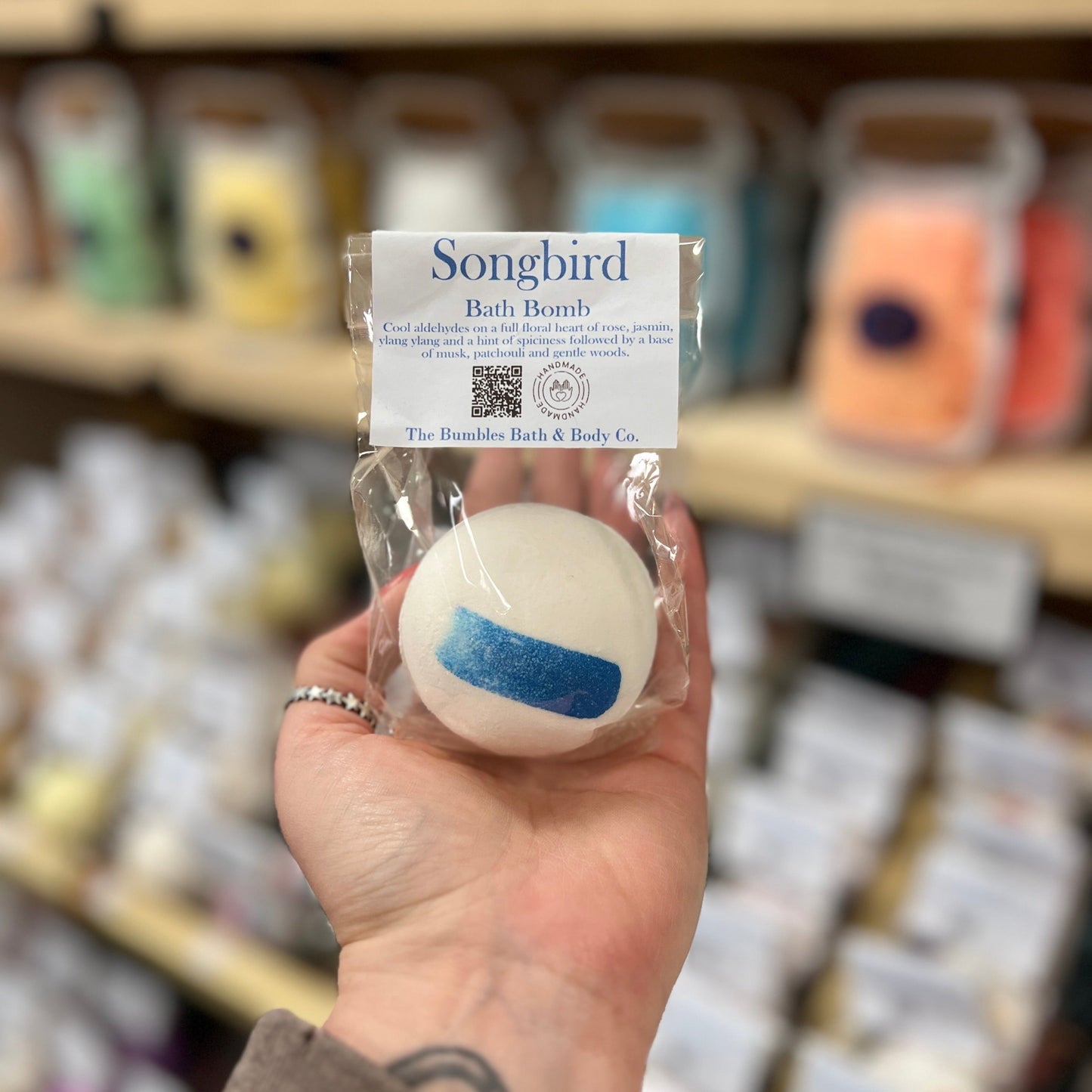 Hand holding a Songbird bath bomb with a blurred store shelf in the background