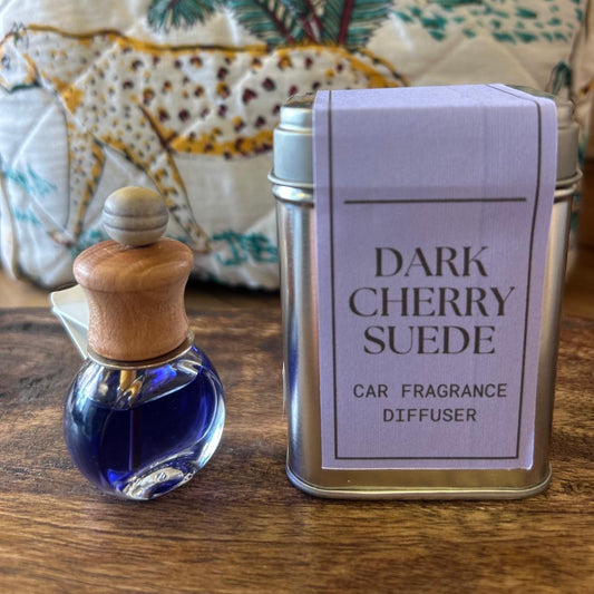 Sage and Bumble Dark Cherry & Suede handcrafted car air freshener. The car air vent diffuser bottle beside metal tin on wooden table