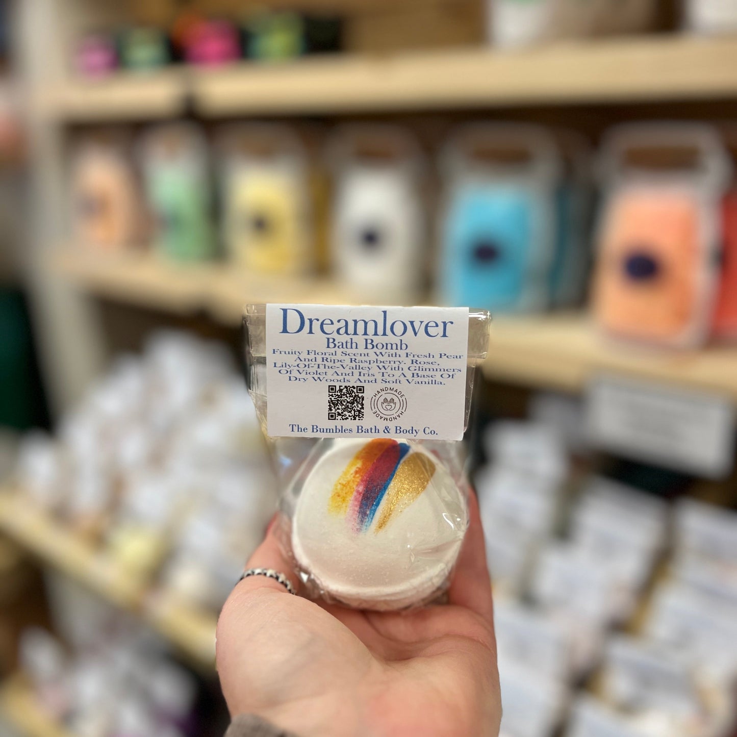 Hand holding a bath bomb labeled 'Dreamlover' in a store setting.