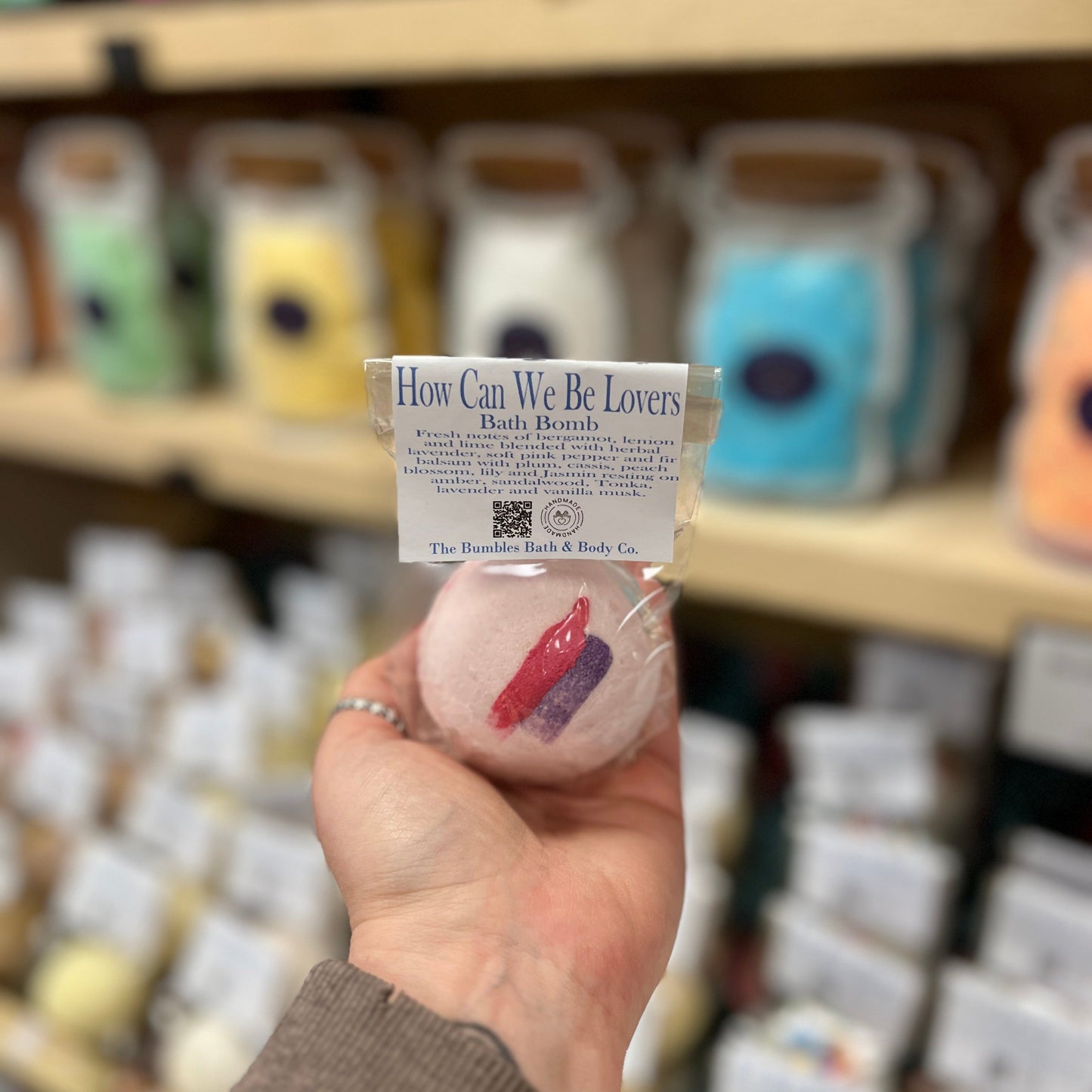 Hand holding a bath bomb with a label in front of shelves with similar products
