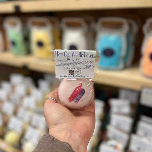 Hand holding a bath bomb with a label in front of shelves with similar products