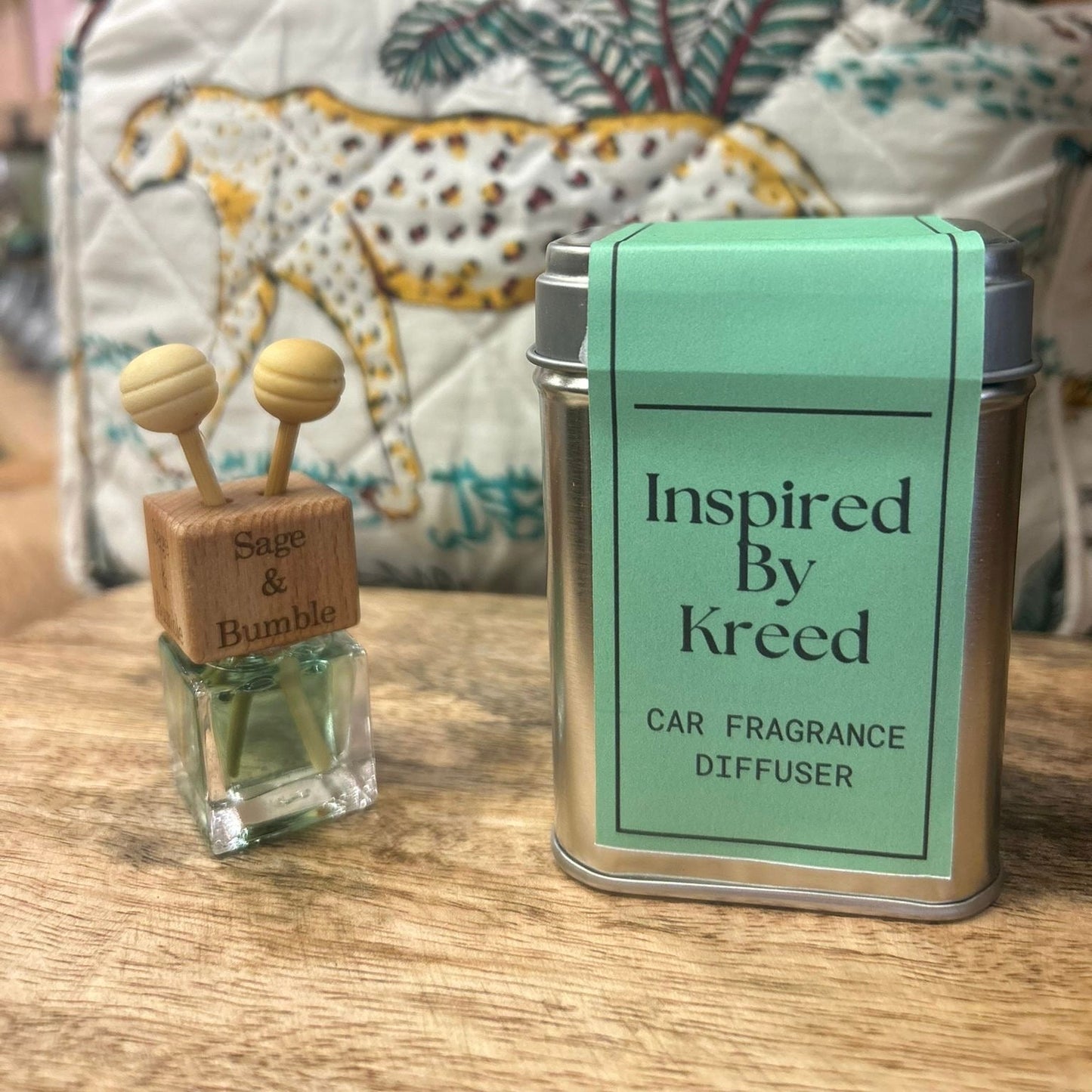 Sage and Bumble Inspired by Kreed handcrafted car air freshener, air vent diffuser bottle beside metal tin on wooden table