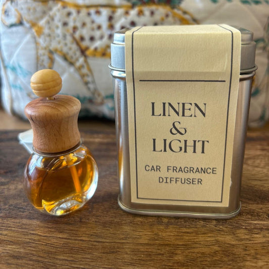 Sage and Bumble Linen Light handcrafted car air freshener.  The car air vent diffuser bottle beside metal tin on wooden table
