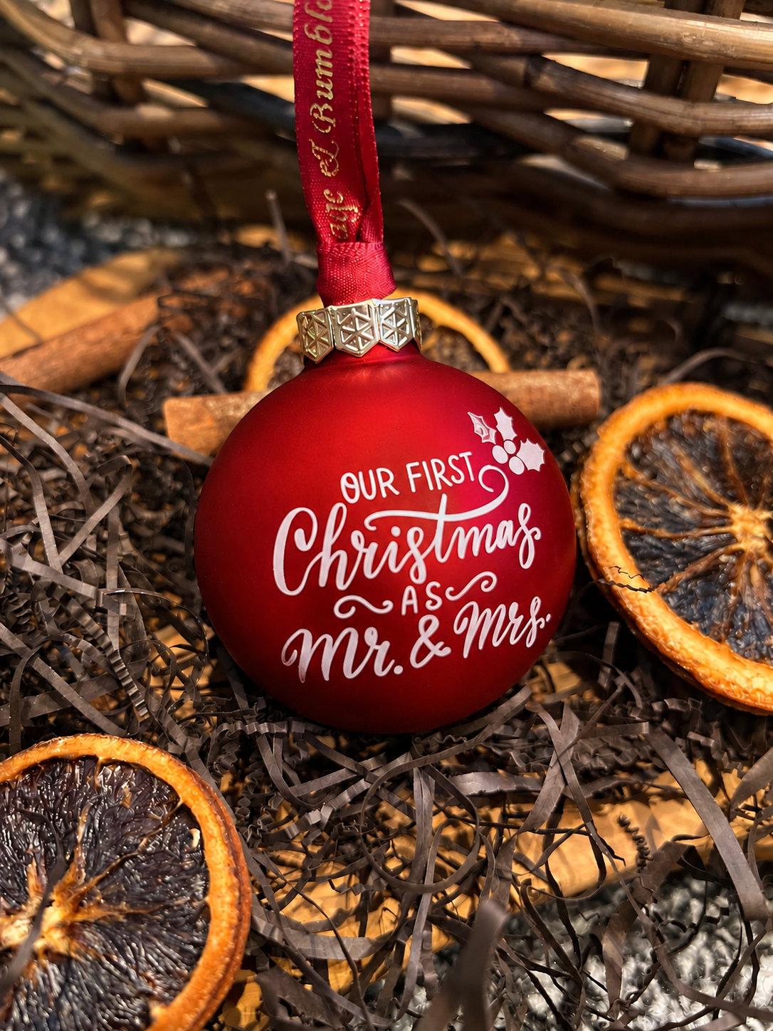 A red Christmas ornament with white script text reading 'OUR FIRST Christmas AS Mr. & Mrs.