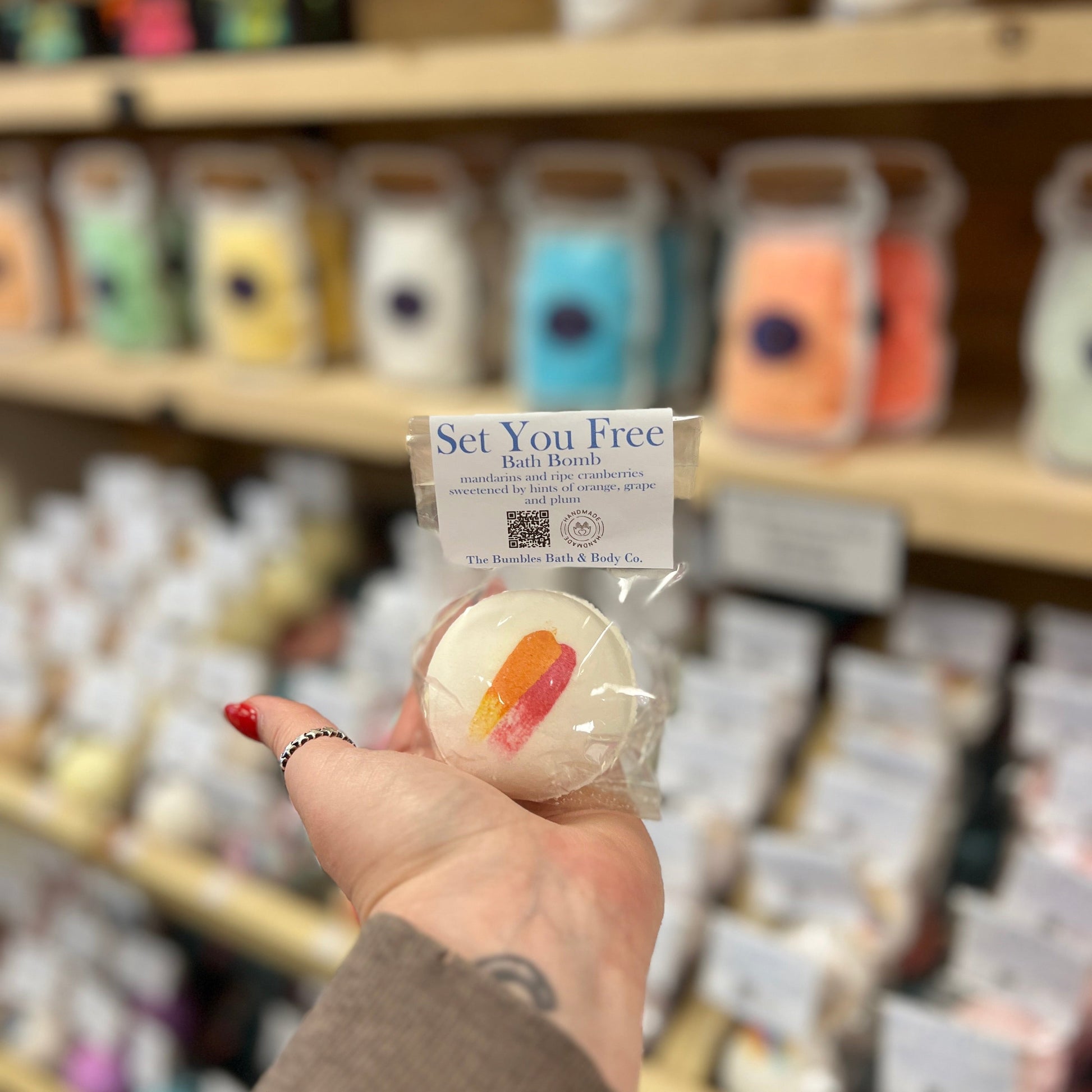 Hand holding a bath bomb labeled 'Set You Free' in a store setting with shelves in the background.