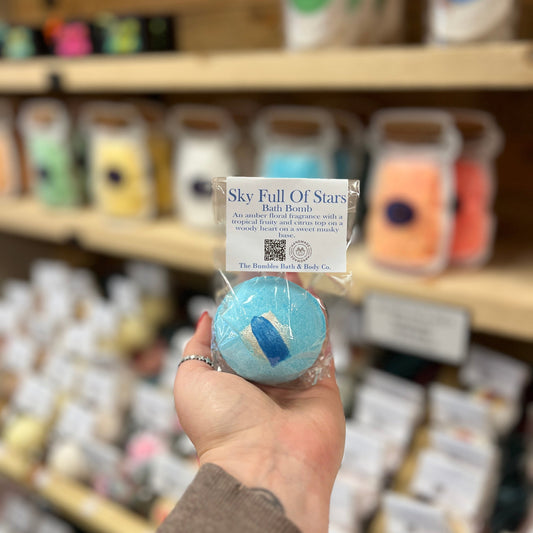 Handmade Blue bath bomb held in front of a store shelf with various products.