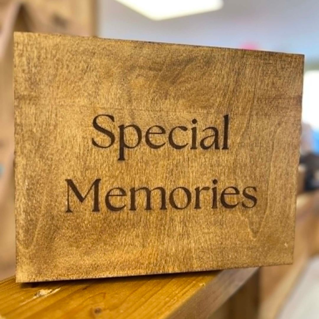 A rectangular wooden sign with the words 'Special Memories' engraved in a dark serif font, resting on a wooden surface with a softly blurred indoor background.